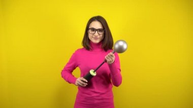 Genç bir kadın, sarı arka planda pompası olan gümüş bir balonu şişiriyor. Pembe balıkçı yaka ve gözlüklü kız..