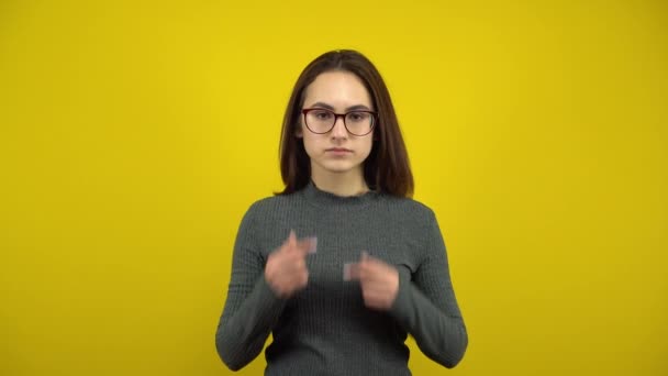 Eine junge Frau macht ein trauriges und fröhliches Lächeln auf ihrem Gesicht, ihre Finger auf gelbem Hintergrund. Frau mit Brille und grünem Pullover. — Stockvideo