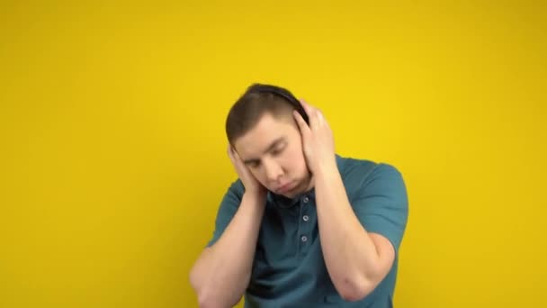 Joven bailando con auriculares sobre un fondo amarillo. Un hombre en un polo verde está escuchando música. — Vídeos de Stock