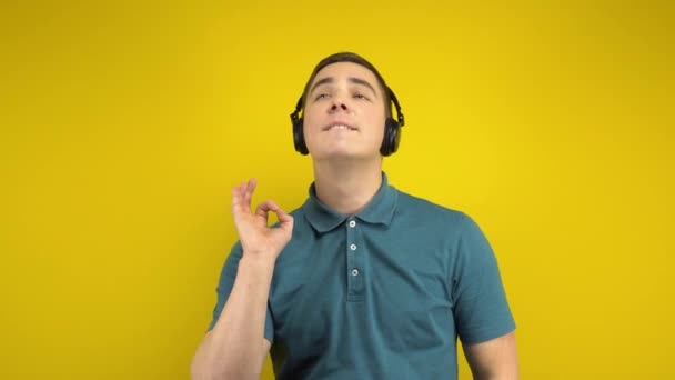 Młody człowiek tańczący ze słuchawkami na żółtym tle. Człowiek w zielonym polo słucha muzyki.. — Wideo stockowe