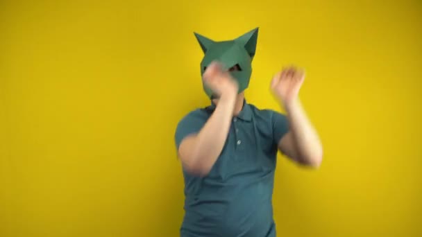 Ung man i en kartong schakal mask dansar på en gul bakgrund. Man i grön polo och mask. — Stockvideo