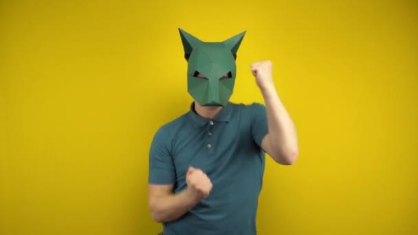 Молодой человек в картонной маске шакала танцует на жёлтом фоне. Человек в зелёном поло и маске. — стоковое видео