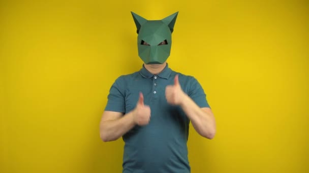 Молодой человек в картонной маске шакала показывает свои пальцы на жёлтом фоне. Человек в зелёном поло и маске. — стоковое видео