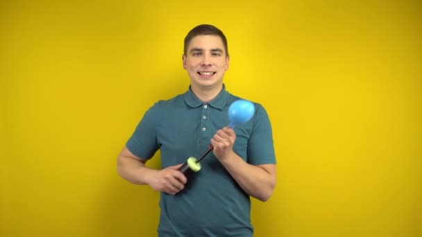 A young man inflates a blue balloon with a pump on a yellow background. Man in a green polo. — Stock Video