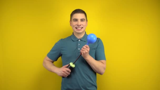 Um jovem infla um balão azul com uma bomba sobre um fundo amarelo. Homem num pólo verde. — Vídeo de Stock