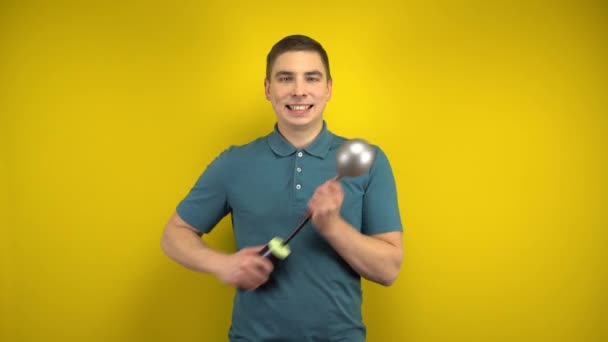 A young man inflates a silver balloon with a pump on a yellow background. Man in a green polo. — Stock Video