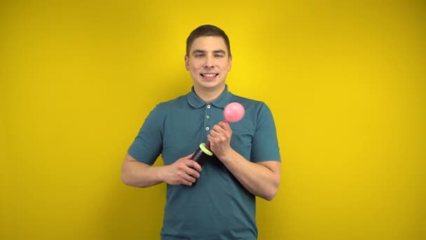 En ung man blåser upp en rosa ballong med en pump på en gul bakgrund. Man i grön polo. — Stockvideo