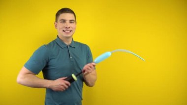 Genç bir adam sarı arka planda pompası olan uzun mavi bir balonu şişirir. Yeşil polo giyen adam..