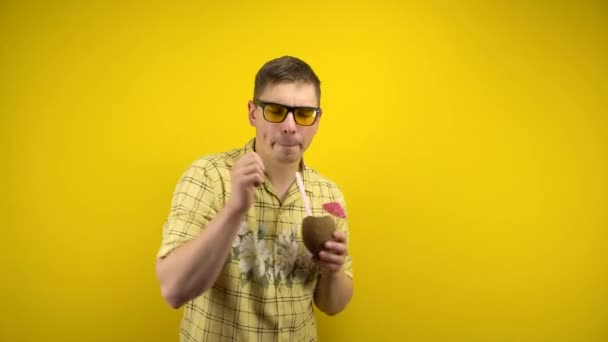 A man in yellow glasses and a Hawaiian shirt is dancing with a coconut pina colada in his hand. Shooting in the studio on a yellow background. — Stock Video