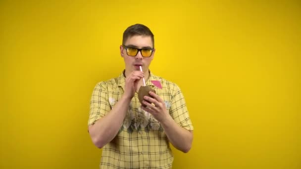 Muž ve žlutých brýlích a havajské košili pije kokosovou piňakoládu a utírá si ruce. Natáčení ve studiu na žlutém pozadí. — Stock video