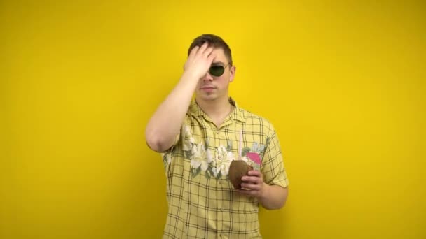 Muž se slunečními brýlemi a havajskou košilí si narovnává vlasy a pije kokosovou pinakoládu. Natáčení ve studiu na žlutém pozadí. — Stock video