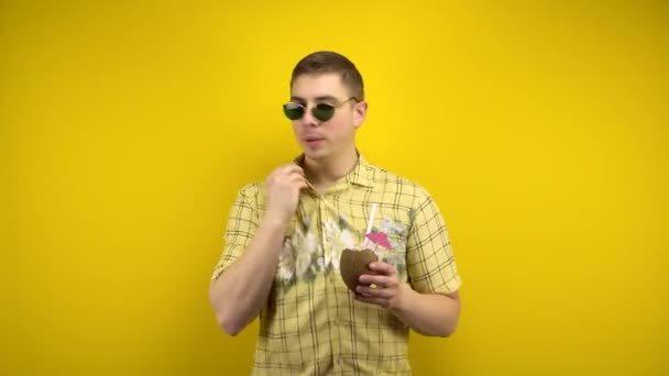 Omul cu ochelari de soare și o cămașă hawaiiană este fierbinte și bea pina colada de nucă de cocos. Impuscaturi in studio pe un fundal galben . — Videoclip de stoc