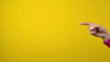Kadın eli, boşluğun işaret parmağını gösteriyor. İzole edilmiş sarı arka planda stüdyo çekimi.