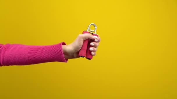 Een vrouwenhand knijpt in een roze expander. Studio fotografie op een geïsoleerde gele achtergrond. — Stockvideo