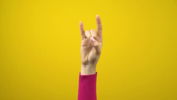 A mão feminina mostra o sinal dos chifres. Fotografia de estúdio em um fundo amarelo isolado. — Vídeo de Stock