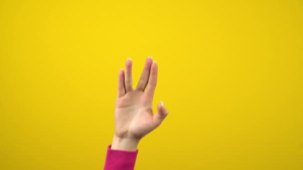 Ένα γυναικείο χέρι δείχνει ένα εξωγήινο σημάδι χαιρετισμού. Φωτογραφία στούντιο σε ένα απομονωμένο κίτρινο φόντο. — Αρχείο Βίντεο