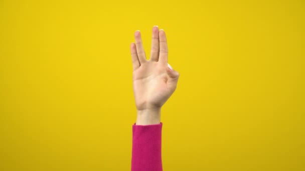 Una mano femenina muestra una señal de saludo alienígena. Fotografía de estudio sobre un fondo amarillo aislado. — Vídeo de stock