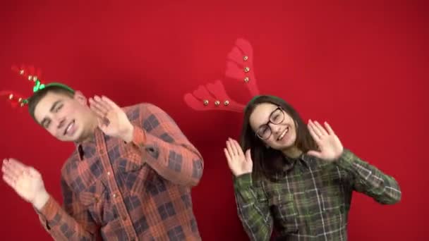 A young woman and a man are dancing with a headband in the form of Christmas deer antlers. Studio shooting on a red background. — Stock Video