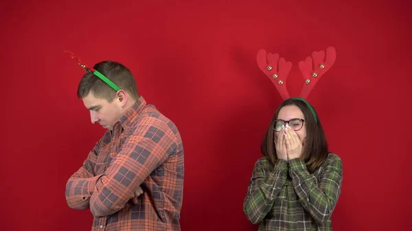 The young woman laughs at the young man because he has small horns and the man is offended against the red background. People wore headbands in the form of deer antlers.