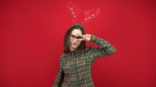 Een jonge vrouw danst met een hoofdband in de vorm van een kerstgewei. Studio schieten op een rode achtergrond. — Stockfoto