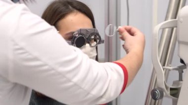 Bir göz doktoru görüşü kontrol eder ve genç bir kadın için farklı lensler takar. Kız virüsten koruyucu bir maske takıyor..