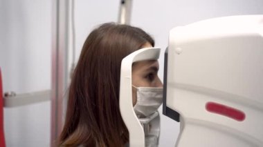 Genç bir kadının görme yeteneği özel bir aletle kontrol edilir. Kız virüsten koruyucu bir maske takıyor..