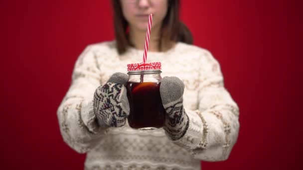 Ung kvinna i vantar sträcker ut glögg till kameran. Fotografering i studion på en röd bakgrund. — Stockvideo