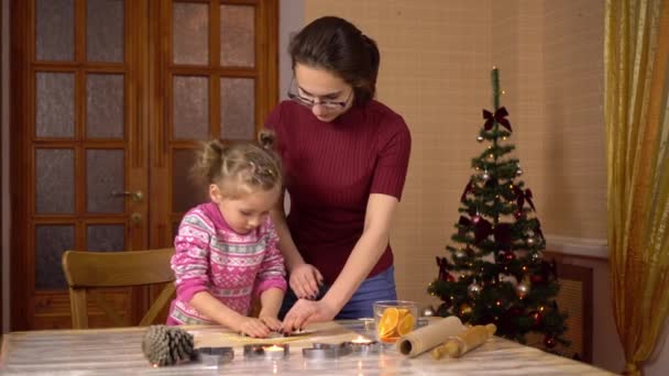 一个女儿和一个年轻的母亲一起做姜饼圣诞饼干。面团里放了一个人偶. — 图库视频影像