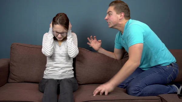 A young man shouts at a young woman. The woman covered his ears with his hands so as not to hear the man. Sitting on the couch — Stock Photo, Image