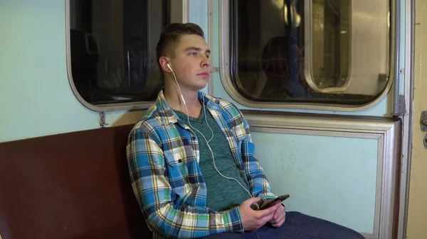 Un joven escucha música con auriculares en un tren subterráneo. Viejo vagón de metro — Foto de Stock