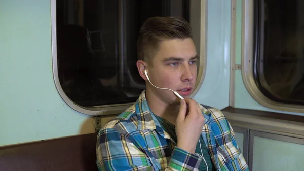 Un joven habla por teléfono a través de auriculares en un tren subterráneo. Viejo vagón de metro — Foto de Stock