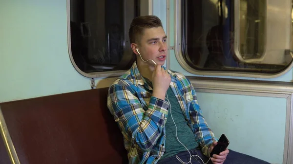 Молодой человек говорит по телефону через наушники в поезде метро. Старый вагон метро — стоковое фото