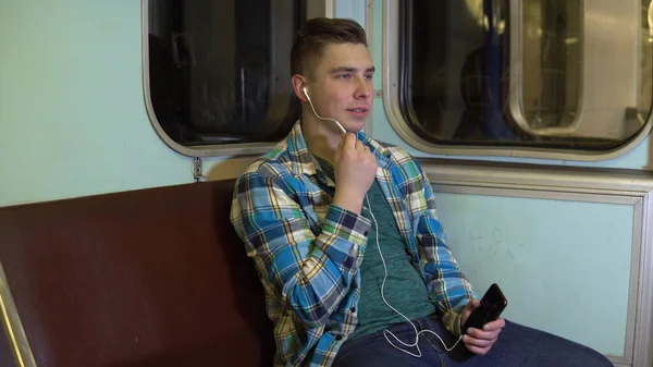 Un joven habla por teléfono a través de auriculares en un tren subterráneo. Viejo vagón de metro —  Fotos de Stock