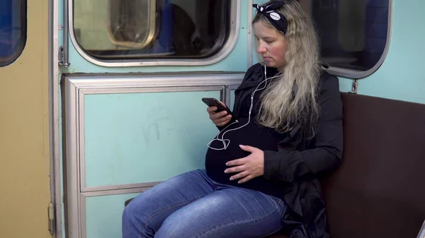 Těhotná žena poslouchá hudbu ve sluchátkách ve vlaku metra. Staré metro vlak auto — Stock fotografie