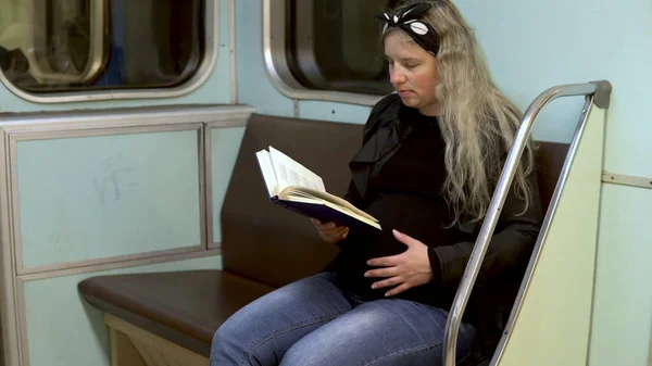 Uma mulher grávida está a ler um livro num comboio do metro. Carro velho do trem do metrô — Fotografia de Stock