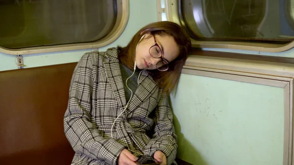 Uma jovem adormeceu num comboio do metro. Rapariga com auscultadores nos ouvidos. Velho carro de metrô — Fotografia de Stock