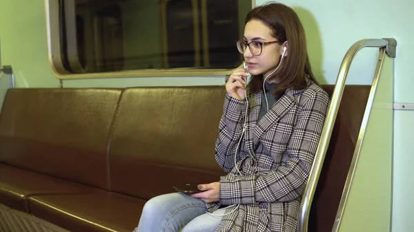 A young woman is talking on the phone through headphones in a subway train. Old subway car — Stock Photo, Image