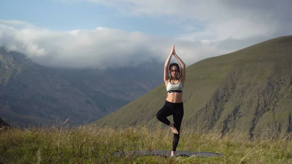 Mujer joven en chándal practica yoga realizando pose de árbol en las montañas. — Foto de Stock