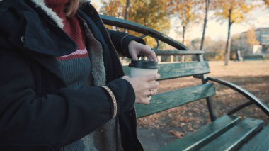 Kız bankta kahve içiyor, yakın plan.