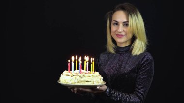 Kız elinde mumlu bir tatil pastası tutuyor. Parlak bir gece elbisesi içinde genç bir kadın duruyor. İzole edilmiş siyah arkaplan