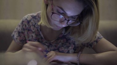 Kız defter notlarına yazıyor. Oturma odasında, masada oturuyor.