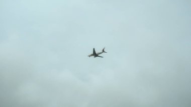 Sisli gri gökyüzünde bir yolcu uçağı uçuyor. Aşağıdan görüntüle.