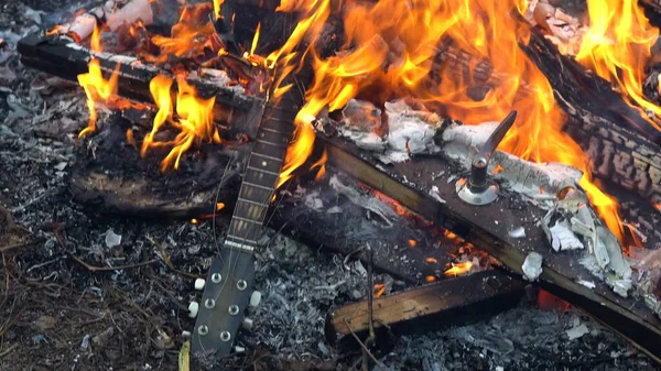 En akustisk gitarr bränns i en stor eld. Brännande skräp. — Stockfoto