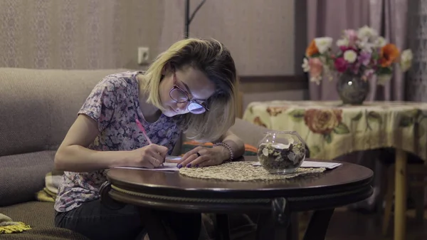 Fata scrie în notele caietului. Stând în camera de zi la masă — Fotografie, imagine de stoc