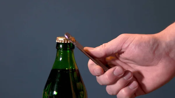 Adam şişeyi özel bir açıcıyla köpüklü içecekle açıyor. Metal kapaklı cam şişe.
