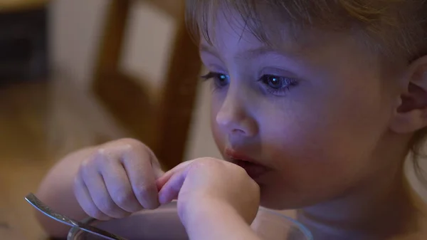 Un enfant mange des boules de chocolat avec du lait et regarde des dessins animés — Photo