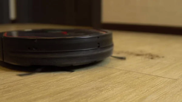 Η σκούπα ρομπότ καθαρίζει το δωμάτιο. Μια στρογγυλή ηλεκτρική σκούπα οδηγεί αυτόματα γύρω από το σπίτι και καθαρίζει τη βρωμιά — Φωτογραφία Αρχείου