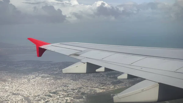 Samolot przelatuje nad miastem w szare chmury. Widok z okna samolotu na skrzydło — Zdjęcie stockowe