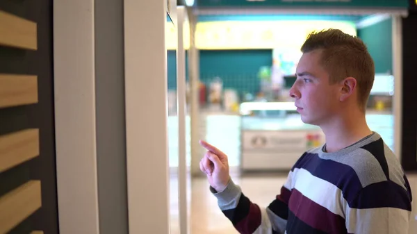 Um jovem pede comida no terminal táctil de um centro comercial. Tecnologia moderna. Na praça de alimentação sem esperar na fila — Fotografia de Stock