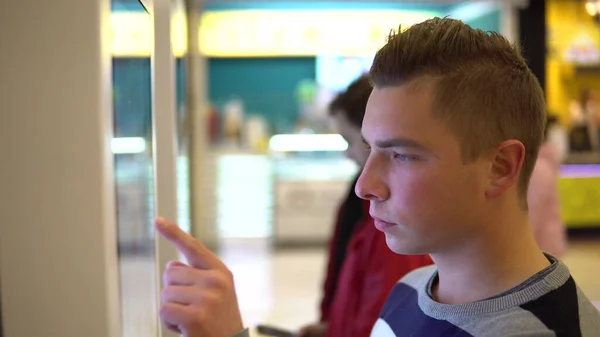 Un joven pide comida en la terminal táctil de un centro comercial. Tecnología moderna. En el patio de comidas sin hacer cola —  Fotos de Stock